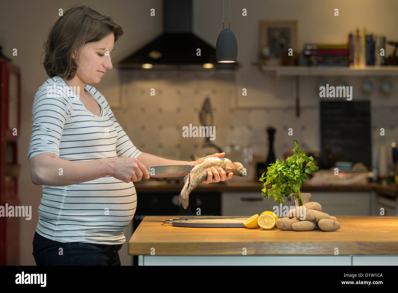 La mujer embarazada, de 35 años, cocinar la trucha fresca en una cocina. Foto de stock