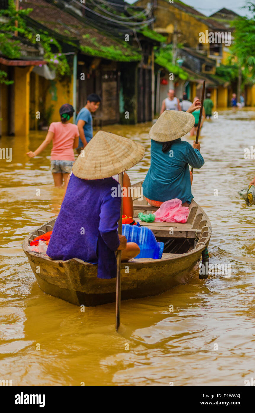 Señoras con sombreros cónicos vietnamitas bote a remo en calle inundada, Hoi An Foto de stock