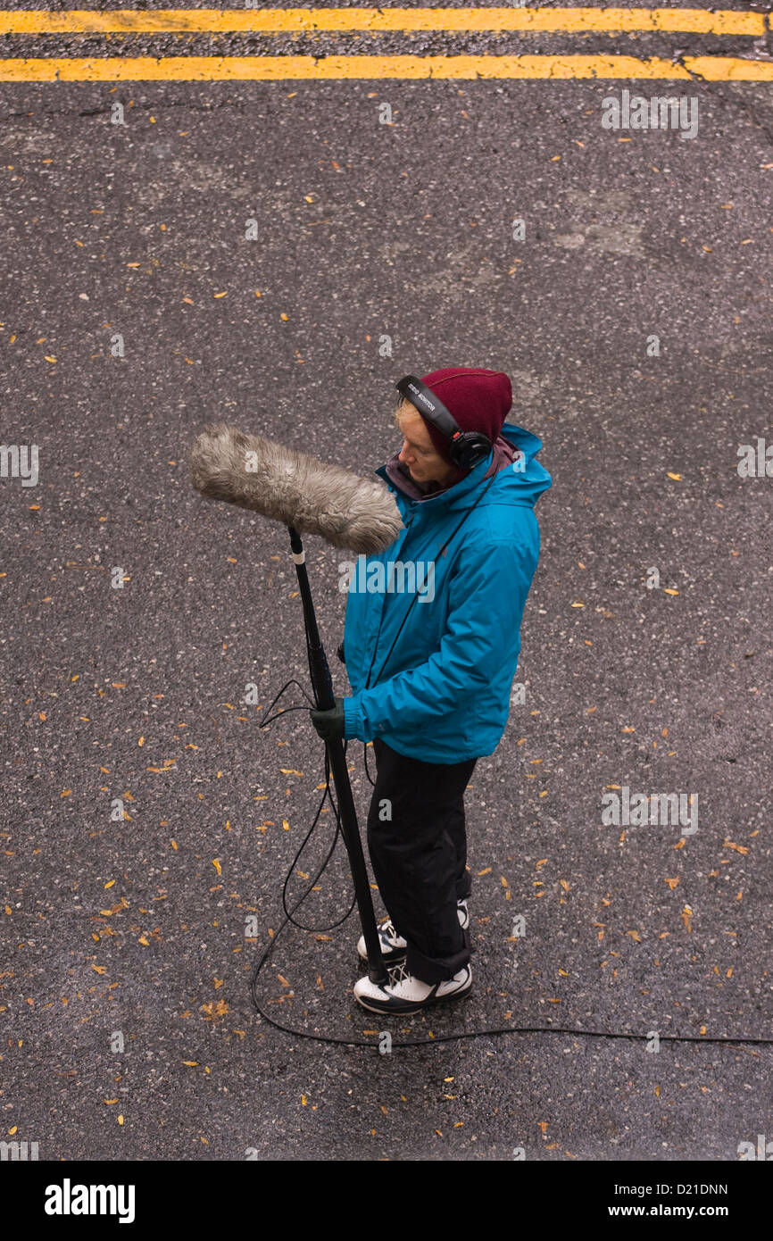 Ingeniero de sonido usando audífonos grabar sonidos en la calle con un micrófono en un boom pole con una piel cubierta de parabrisas Foto de stock