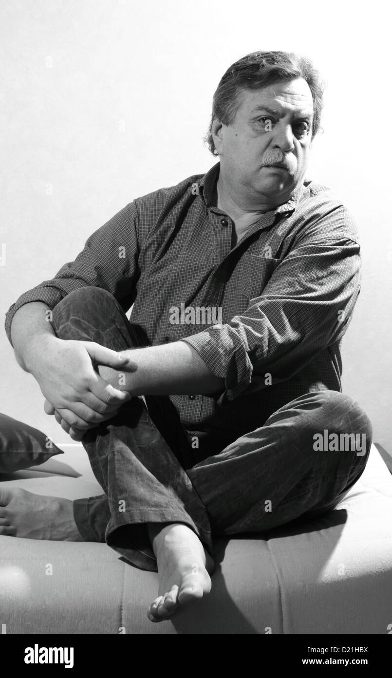 Retrato en blanco y negro de hombre de edad midle asientos sofá Foto de stock