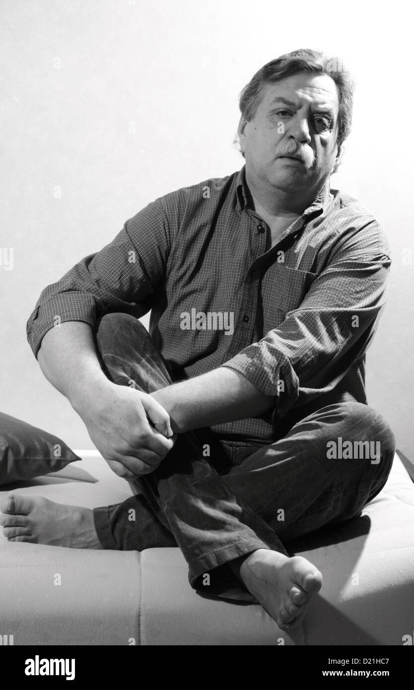 Retrato en blanco y negro de hombre de edad midle asientos sofá Foto de stock