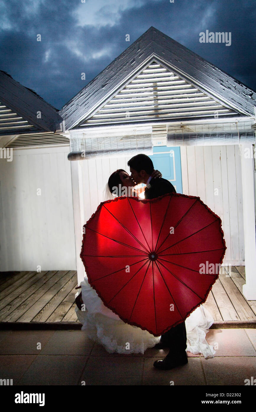 Pareja con un paraguas rojo besando en un parque rodeado por el verdor y  una cascada Fotografía de stock - Alamy