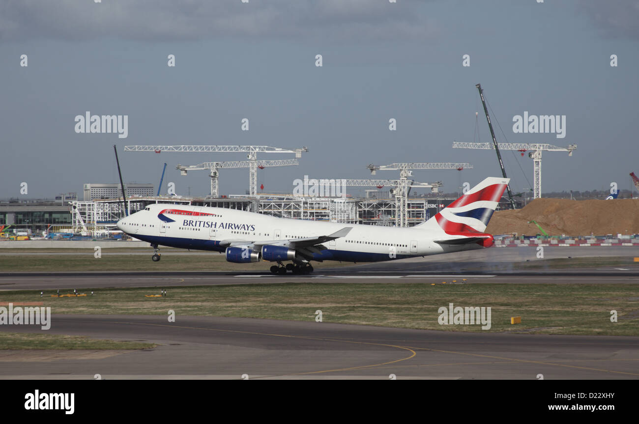 Boeing 747 de British Airways aterrizando en el aeropuerto de Heathrow en Londres; la construcción del terminal funciona en segundo plano. Foto de stock