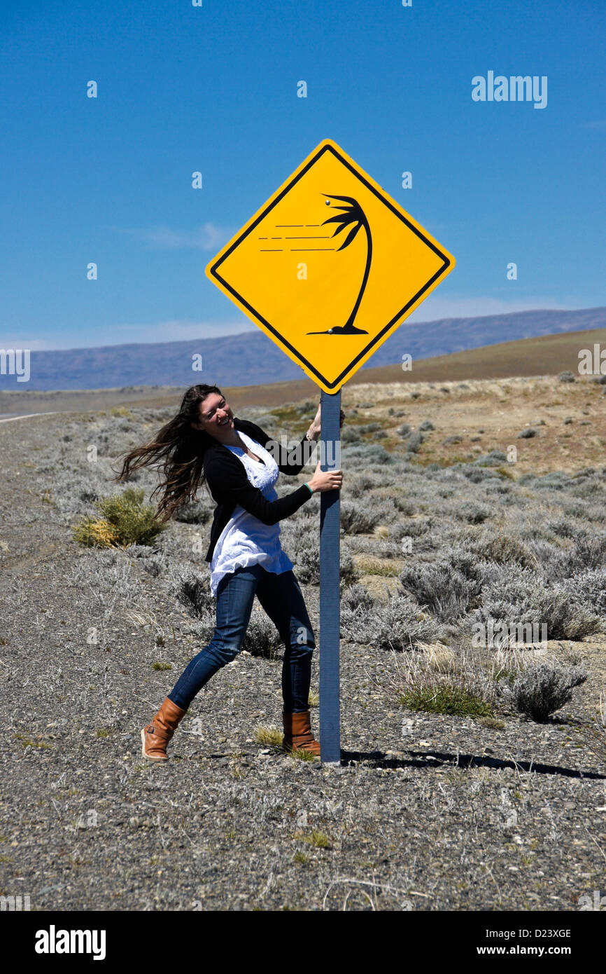 Chica colgando de señales de advertencia de viento fuerte, Patagonia, Argentina Foto de stock
