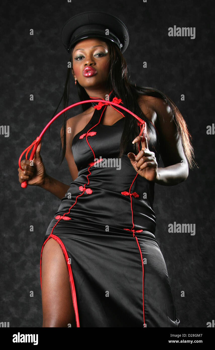 África negra mujer vistiendo un traje negro y rojo chino, tapa negra y blandiendo una fusta roja. Foto de stock
