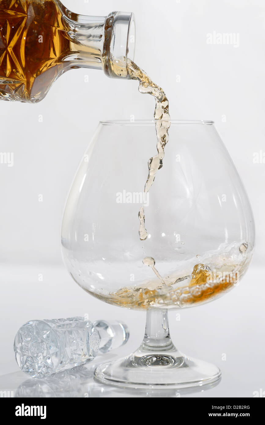 Alta velocidad de gotas congeladas de verter el brandy de un decantador de cristal en un vidrio snifter sobre fondo blanco. Foto de stock