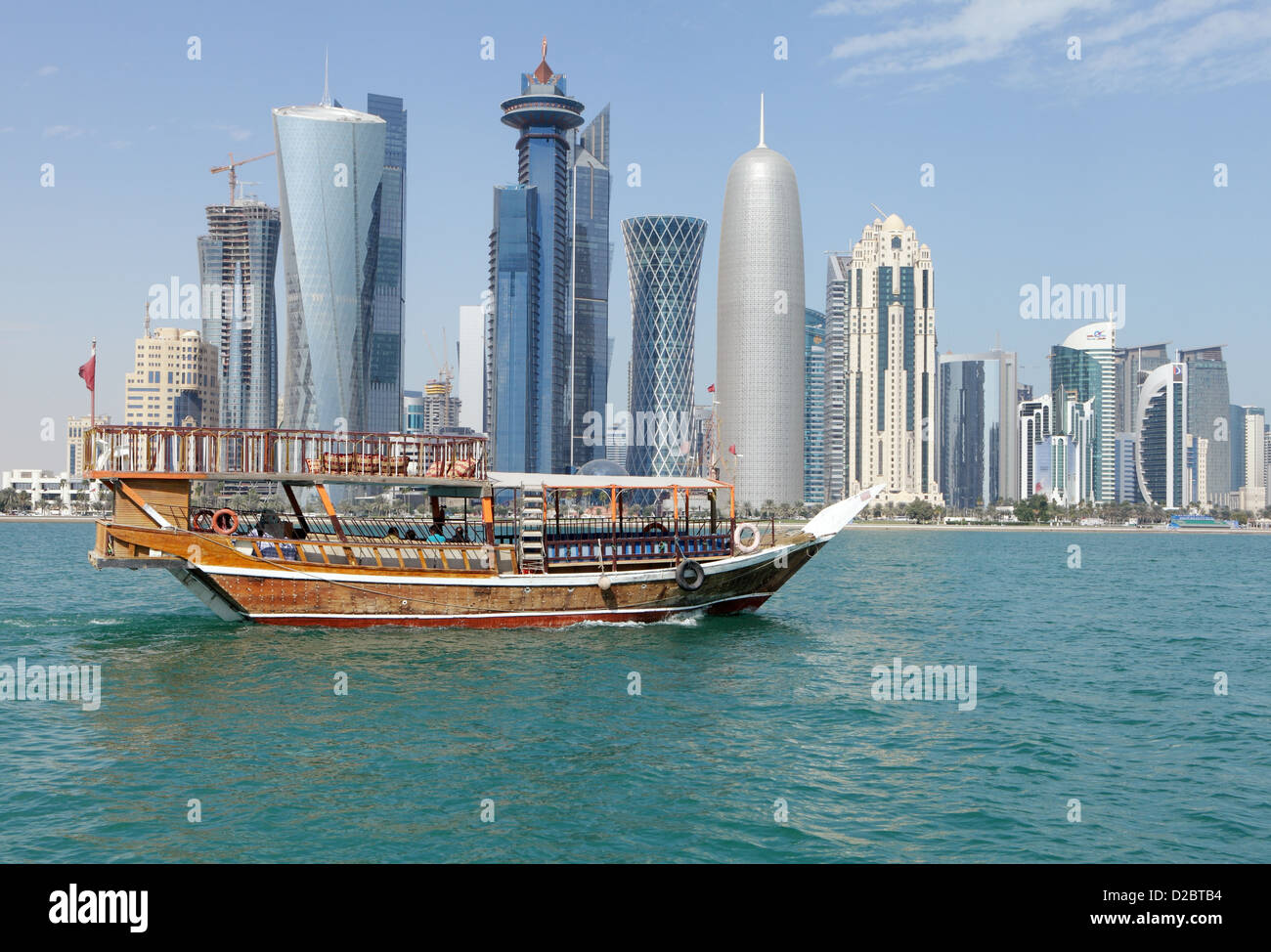 Un Dhow navegando por la bahía de Doha con las torres de los rascacielos Dafna distrito en el fondo y algunas nubes Foto de stock
