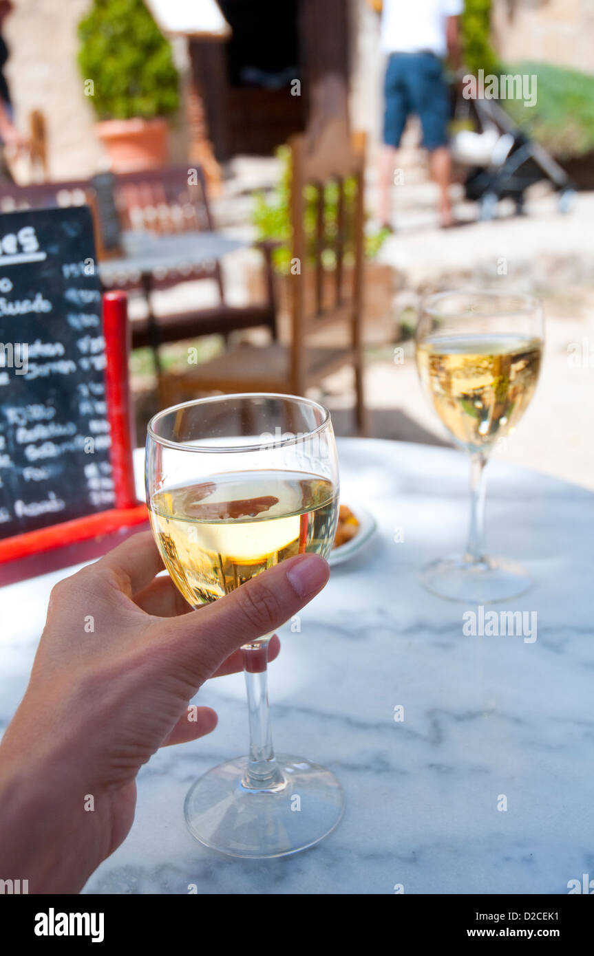 Mano de mujer sosteniendo un vaso de vino blanco en una terraza. Pedraza, provincia de Segovia, Castilla y León, España. Foto de stock