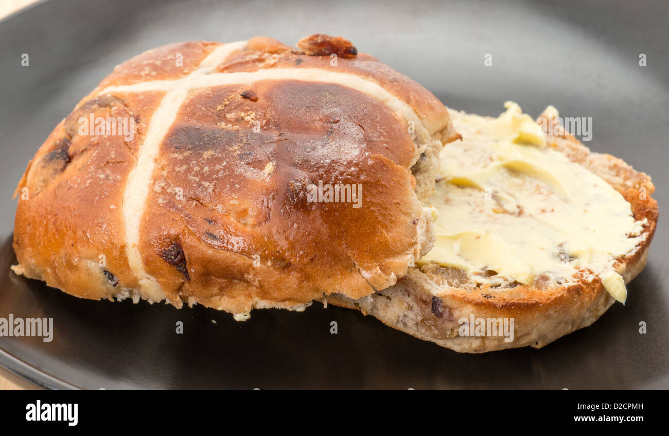 Close-up de una tostada con mantequilla y hot cross bun servido en un plato de té negro Foto de stock