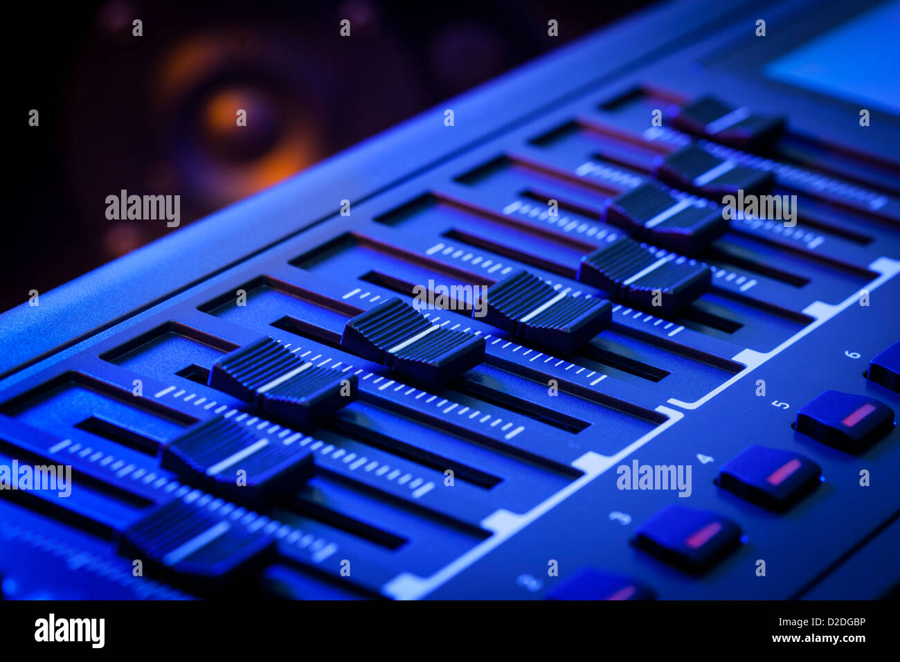 Close-up de una fila de deslizadores de control sobre un teclado controlador MIDI con un altavoz fuera de foco en el fondo. Foto de stock