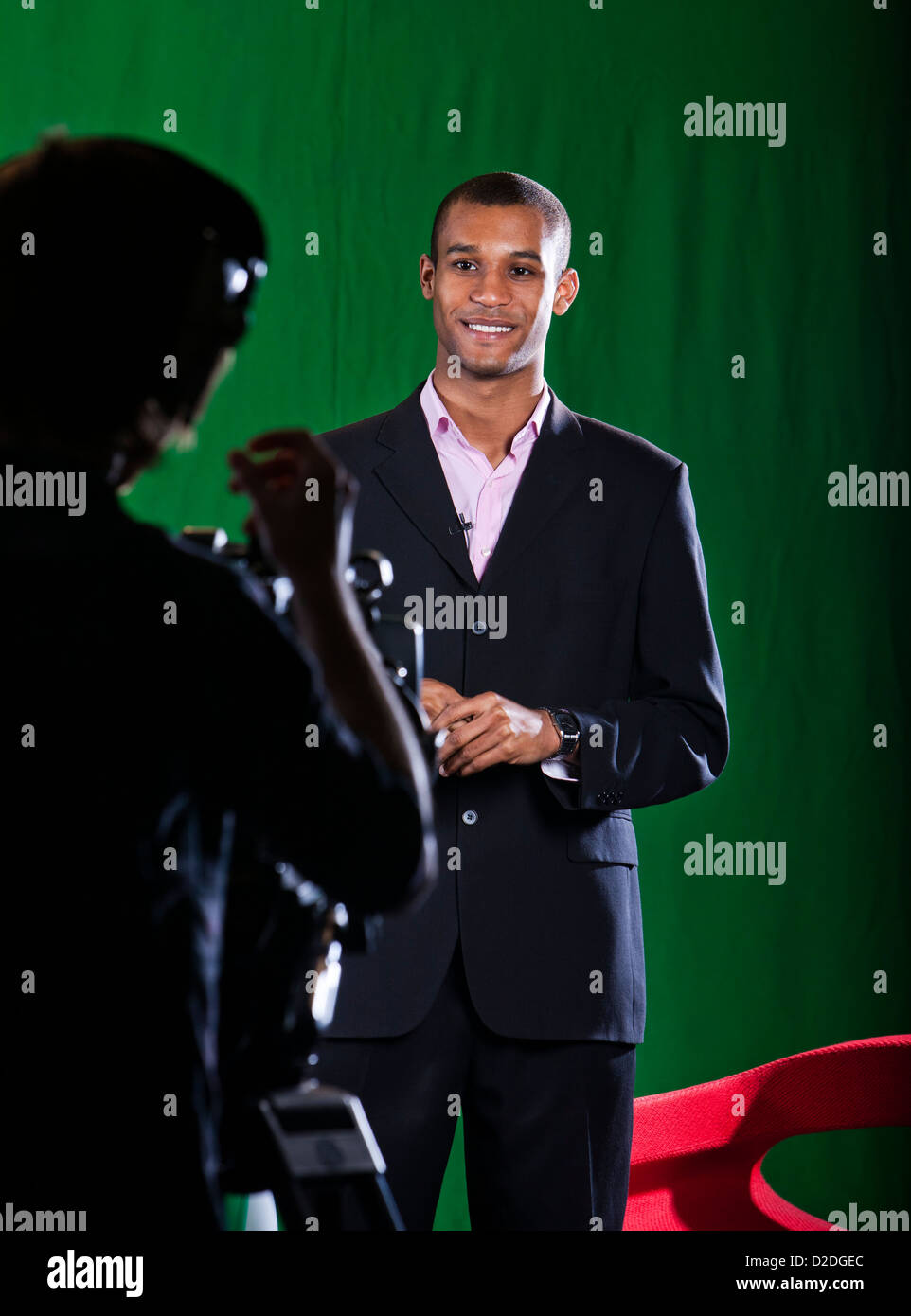 Presentador en un estudio de televisión de pantalla verde chats con un operador de cámara silueteado en primer plano. Foto de stock