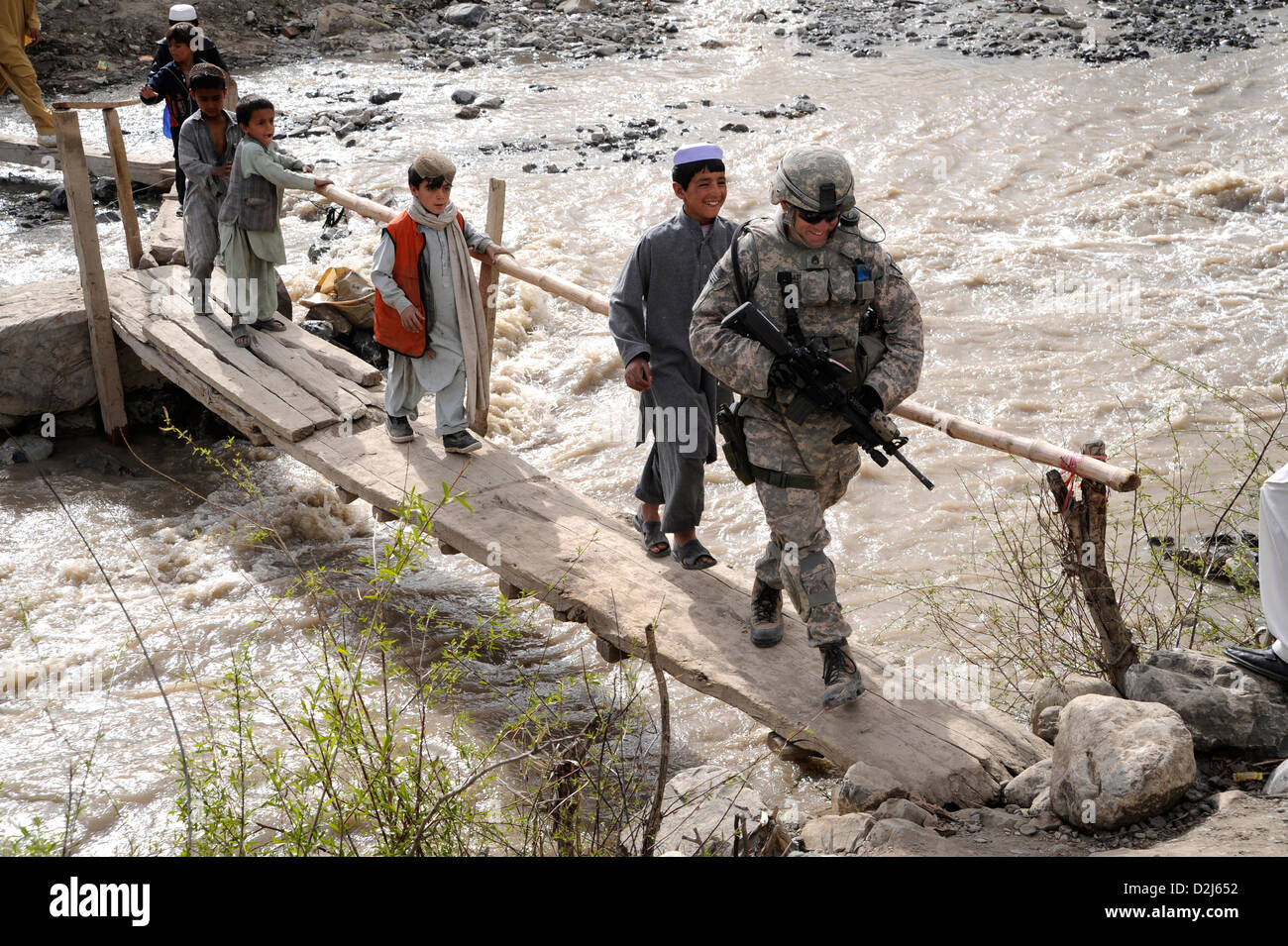Los niños afganos siguen un soldado estadounidense a través de un puente en una aldea cerca de la base de operaciones avanzada Herrera, Afganistán, 18 de abril de 2009. Foto de stock