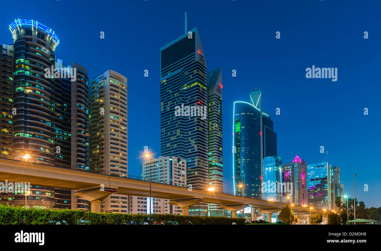 Horizonte de Dubai, Emiratos Árabes Unidos, el Jeque Zayed Rd, en la noche con una línea de tren y metro de elevados rascacielos Foto de stock