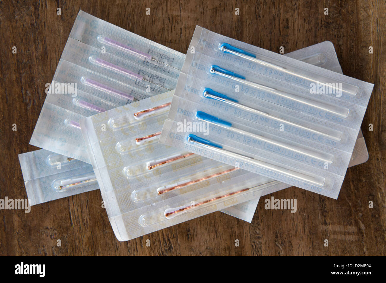 Surtido de diferentes tamaños de agujas de acupuntura en paquetes sellados adoptadas sobre una mesa de madera Foto de stock