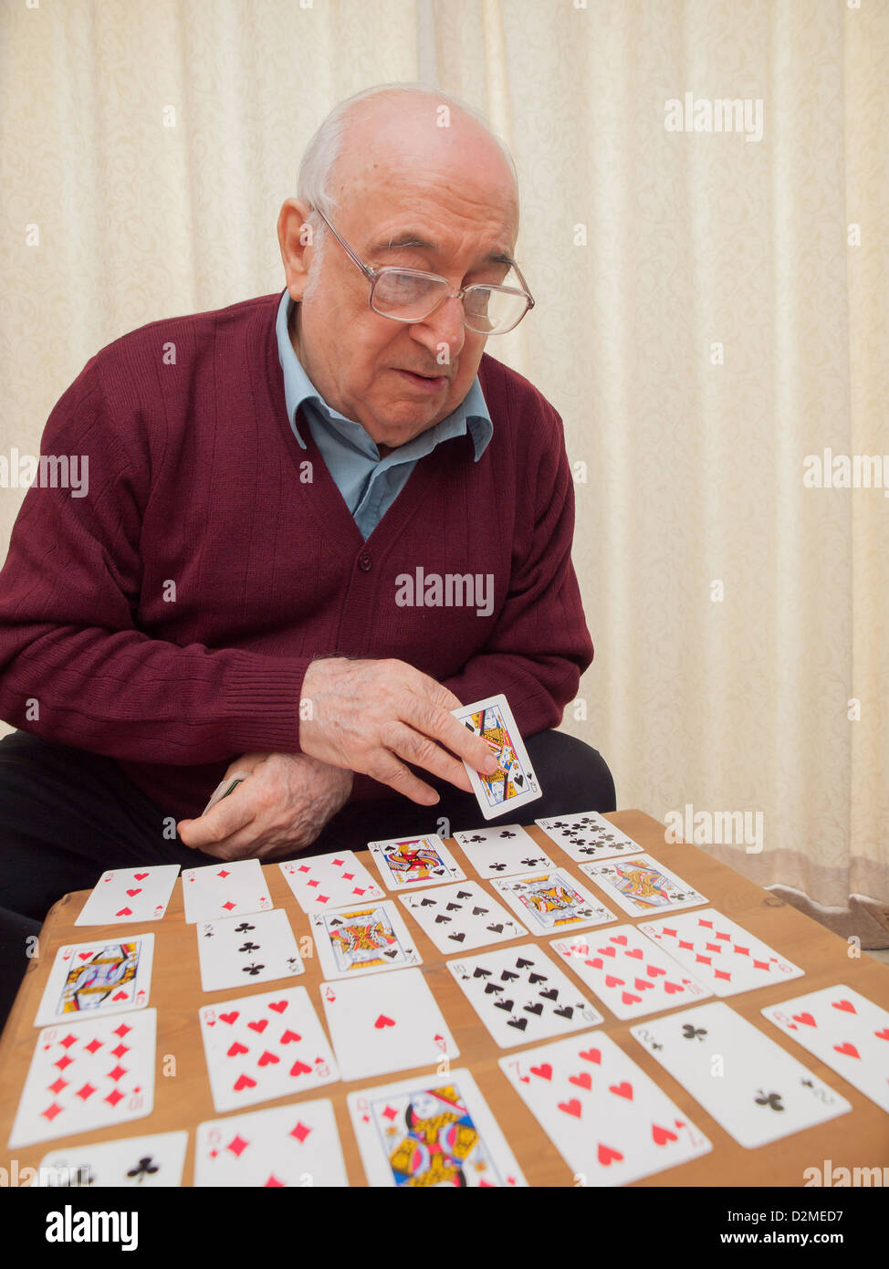 Ancianos hombre sentado jugando a las cartas en su propio Foto de stock
