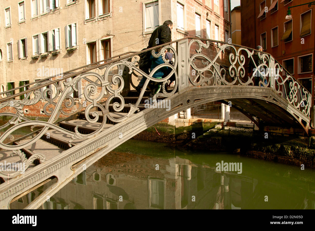 Puente de metal excepcional a lo largo de un canal con reflejos de agua y peatonal, Venecia, Véneto, Italia Foto de stock