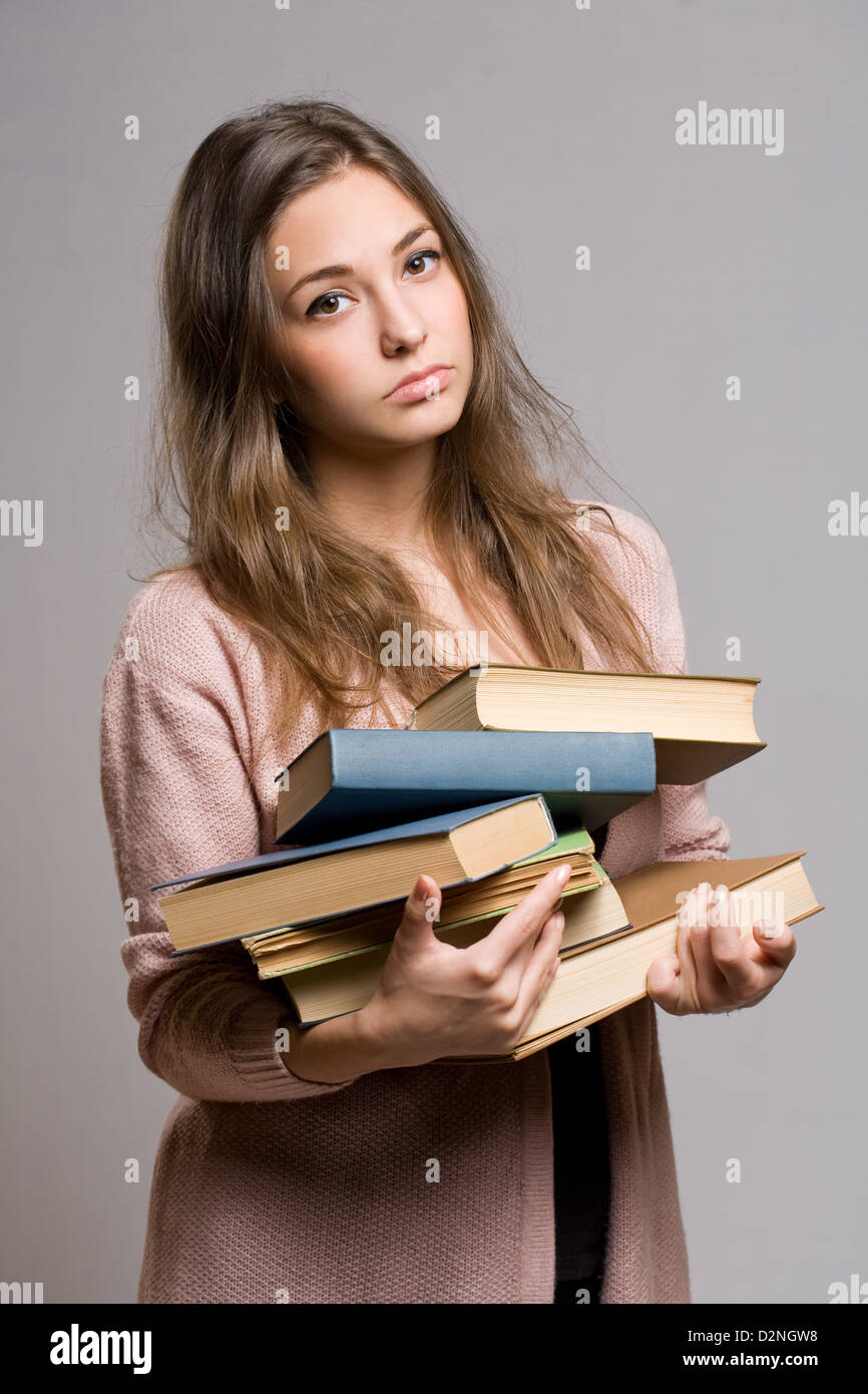 Retrato de malgastado buscando chica joven estudiante llevar gran montón de libros. Foto de stock