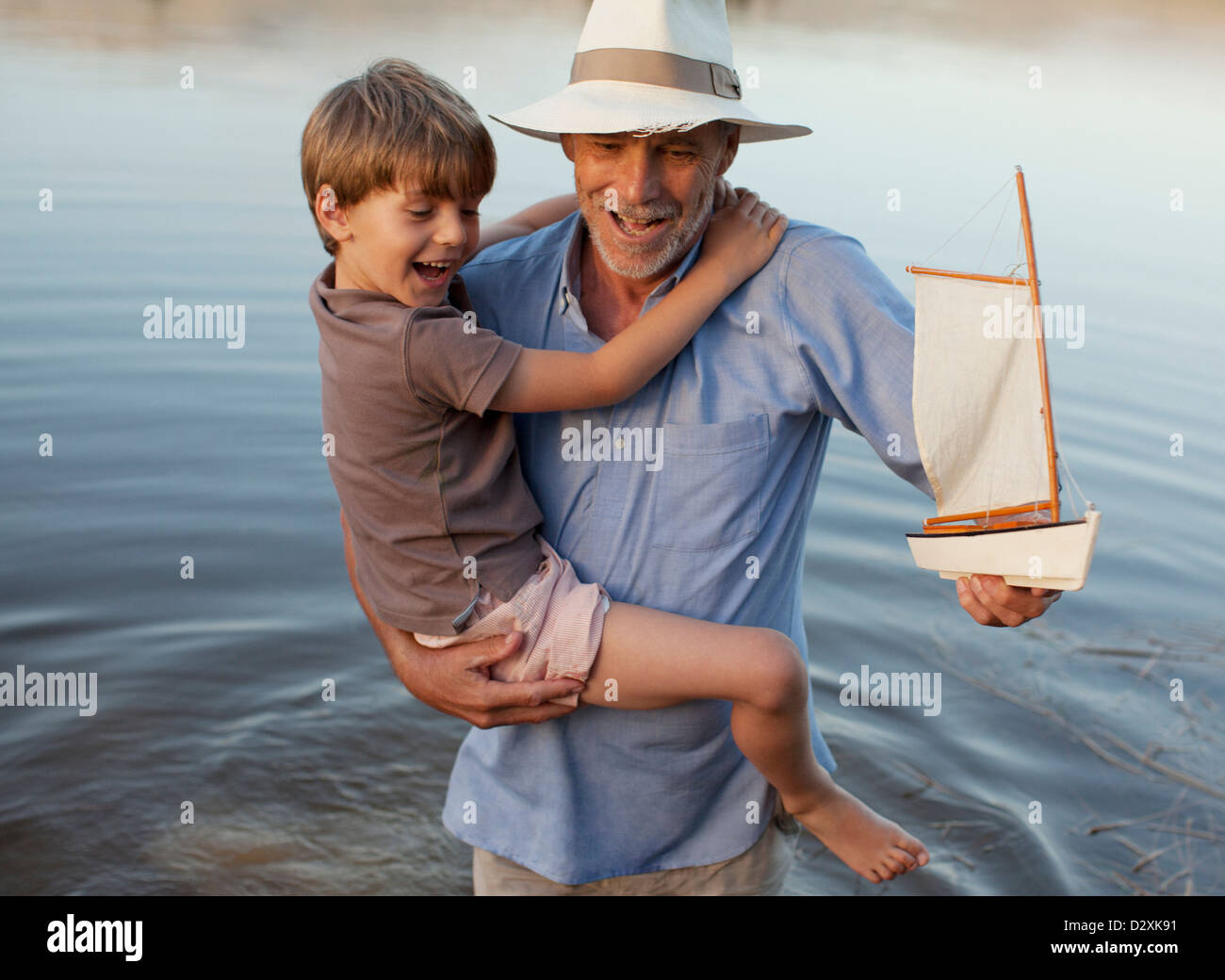 Sonriente, abuelo y nieto de juguete con velero vadeando en el lago Foto de stock