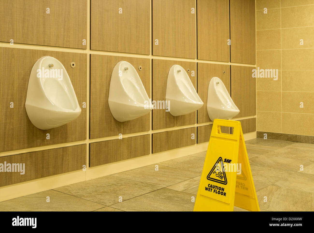 Hilera de urinarios y piso mojado firmar en los aseos Foto de stock