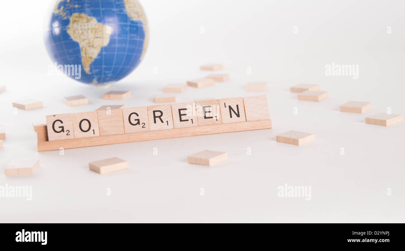 'Go Green' escrito en letras de Scrabble con fuera de foco en el fondo plano del mundo. Aislado sobre fondo blanco. Foto de stock