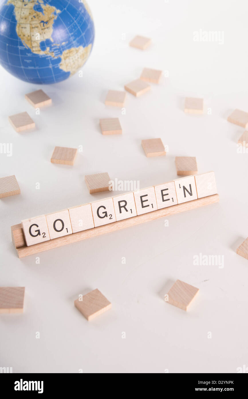 'Go Green' escrito en letras de Scrabble con fuera de foco en el fondo plano del mundo. Aislado sobre fondo blanco. Foto de stock