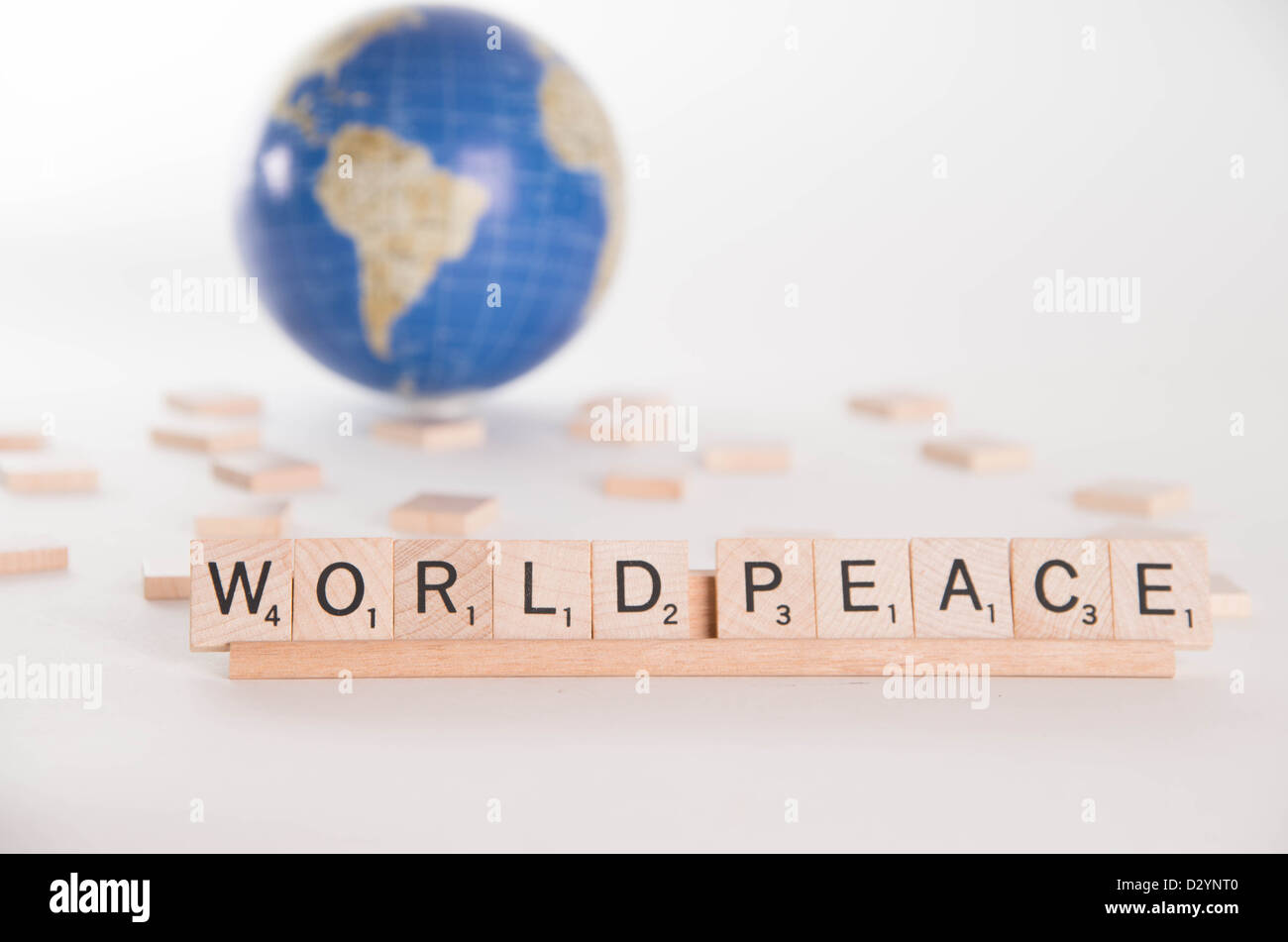 Concepto: "La paz mundial" escrito en letras de Scrabble con fuera de foco globe en segundo plano. Aislado sobre fondo blanco. Foto de stock