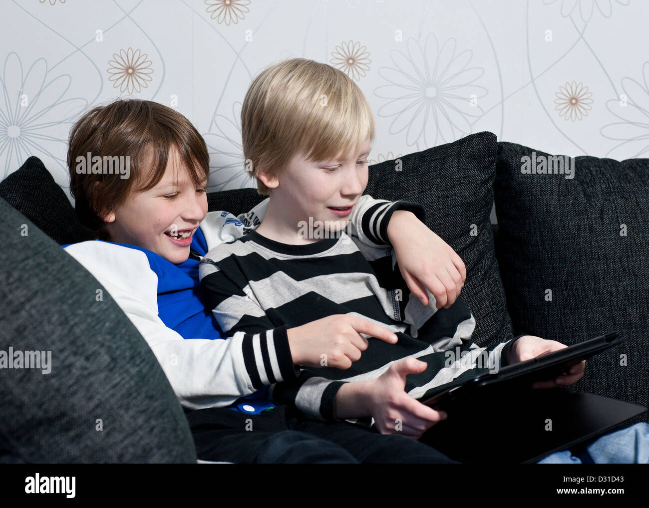 Dos niños en un sofá divirtiéndonos juntos con un equipo tablet pc Foto de stock