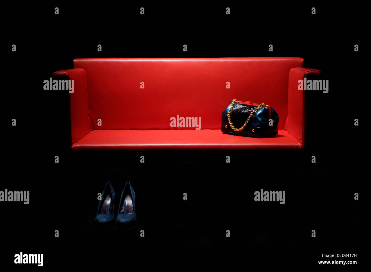 Sofá de cuero rojo con bolsos y calzados femeninos. Foto de stock