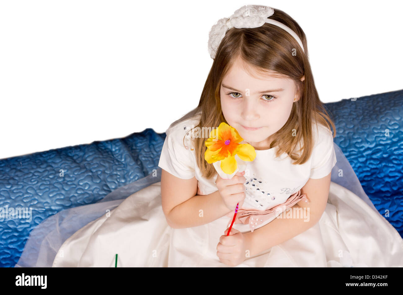 Un alto ángulo de visualización de una hermosa niña la celebración de un único color naranja flor artificial a su mejilla vistiendo un arco en su pelo con copyspace. Foto de stock