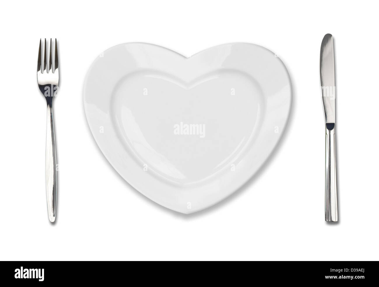 Placa en forma de corazón, cuchillo y tenedor de mesa aislado en blanco Foto de stock