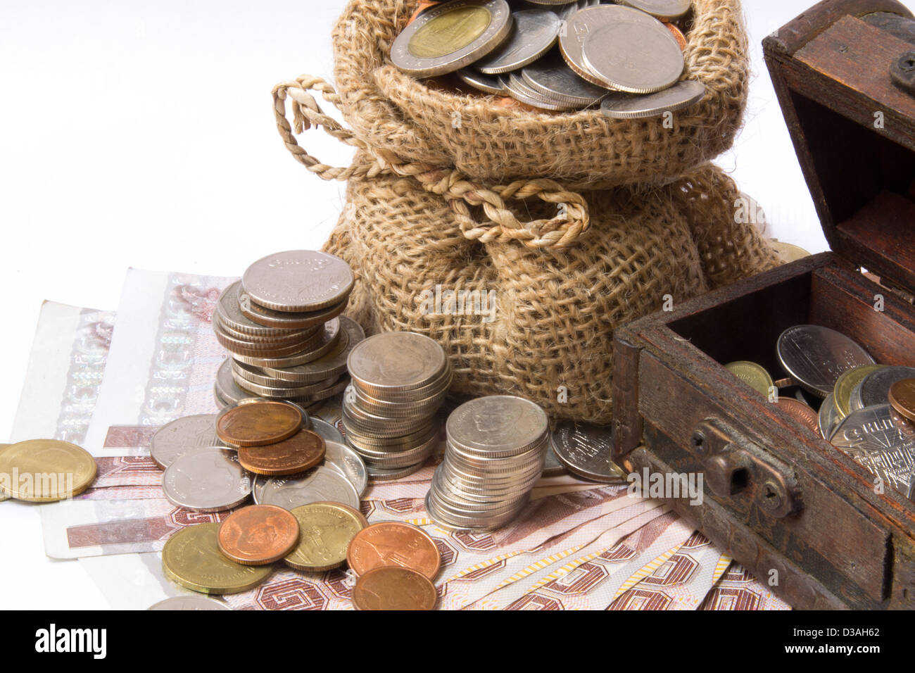 Dinero monedas en la bolsa y pecho de madera aislado en blanco Foto de stock