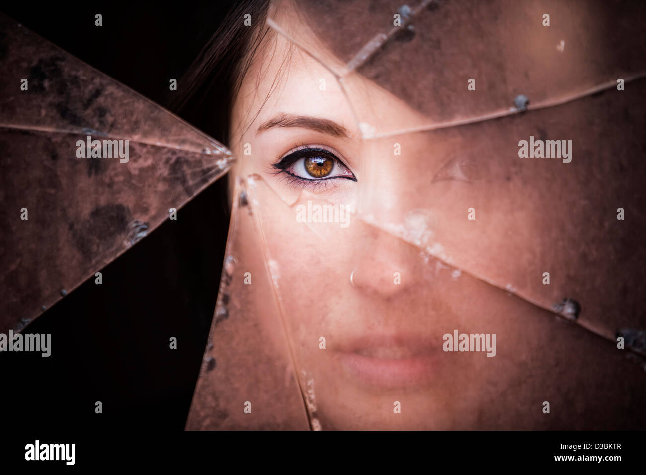Mujer mirando a través del vidrio roto sucio Foto de stock