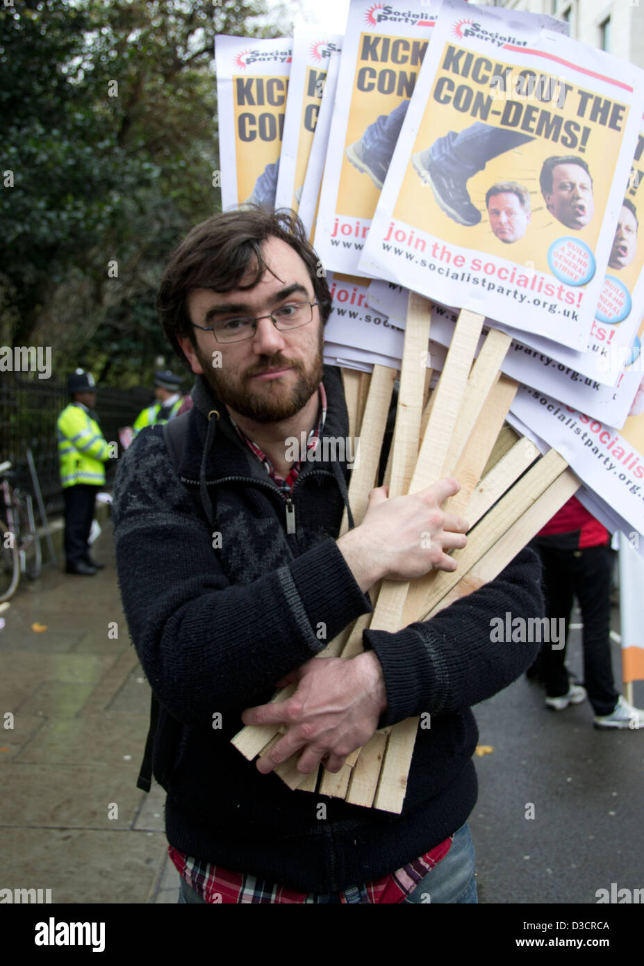 Hombre con gafas sosteniendo pancartas de protesta 'kick out la con-dems' en Londres protesta estudiantil 2012 con la policía en el fondo. Foto de stock