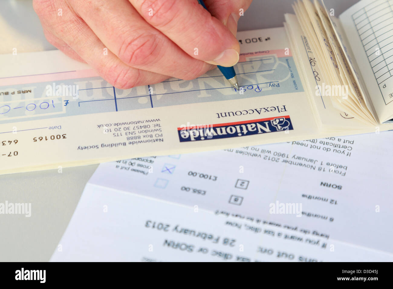 Persona del sexo femenino escribir un cheque para pagar en todo el país durante 12 meses coche renovación fiscal en la oficina de correos. Inglaterra Gran Bretaña Foto de stock