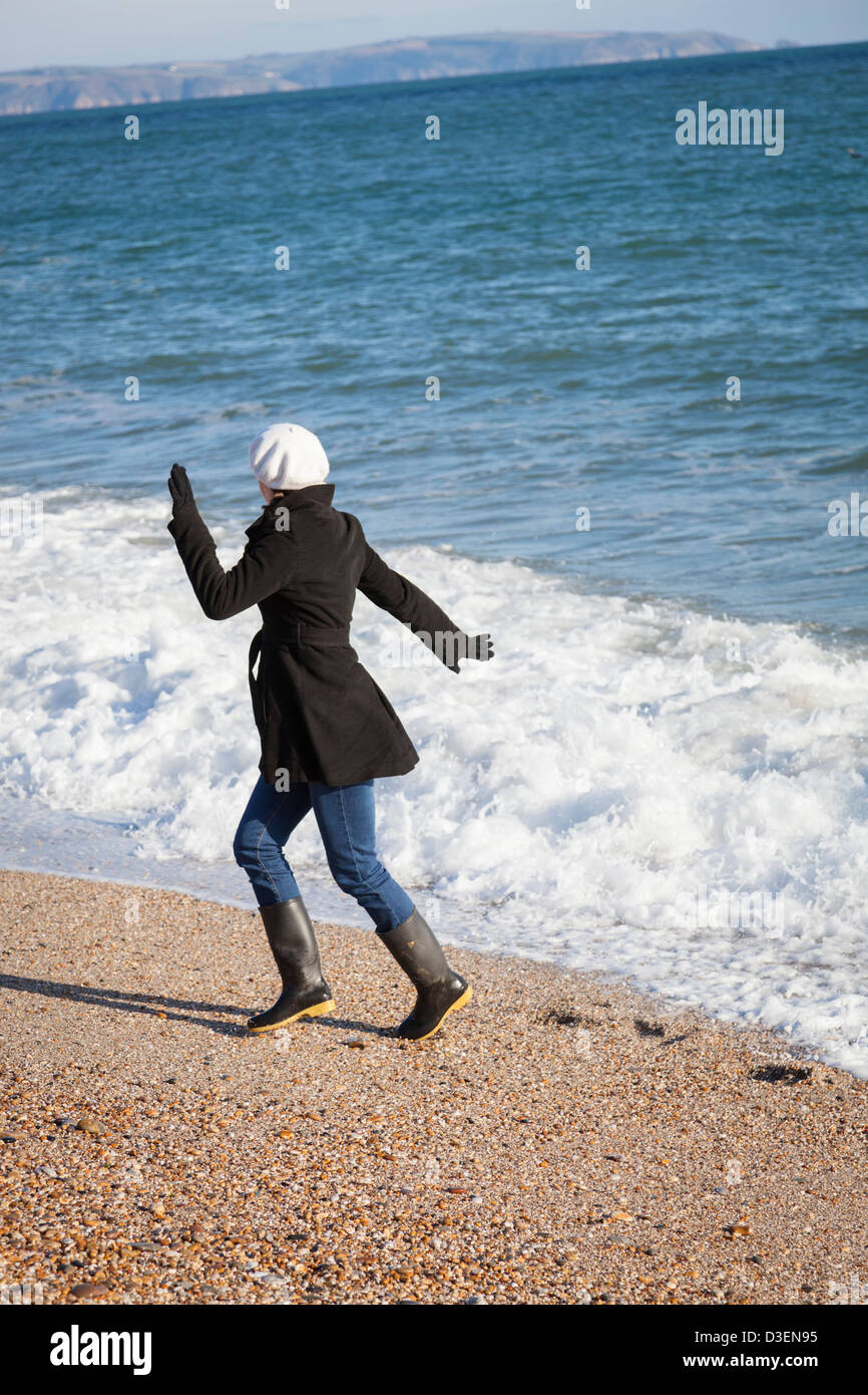 Vestida de ropa de invierno y botas Wellington jugando en las olas en la  playa Fotografía de stock - Alamy