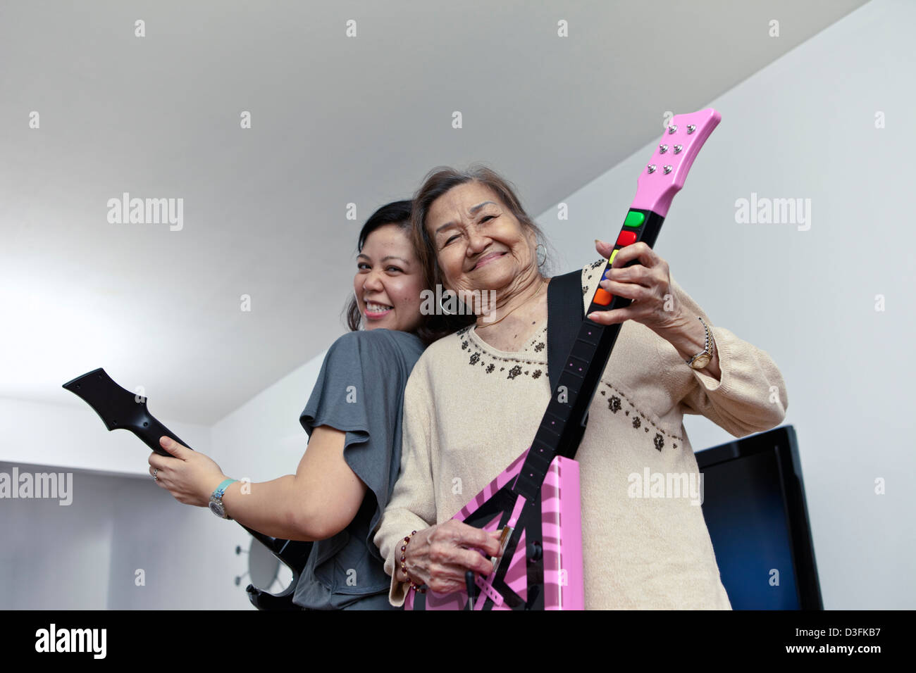 Dos generaciones de mujeres asiáticas en familia divirtiéndose tocando la guitarra juego electrónico Foto de stock