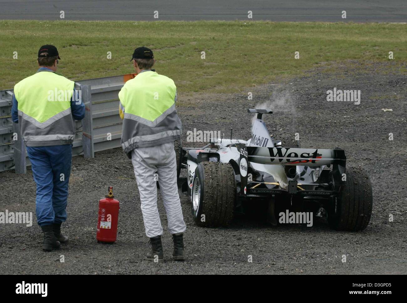 (Dpa) - Dos vía marshalls pararse junto al vapor de coche de carreras de Fórmula uno finlandés Kimi Raeikkoenen piloto de McLaren-Mercedes tras un fallo de motor al europeo durante el Grand Prix de F1 en la pista de Nurburgring, Alemania, 30 de mayo de 2004. Foto de stock