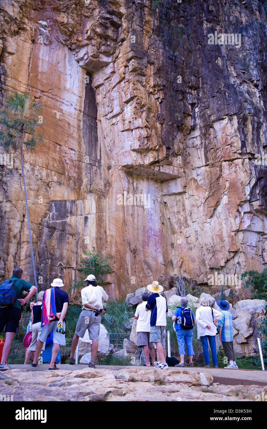 Los turistas una pausa para echar un vistazo a un grupo de arte rupestre aborigen antigua en un acantilado de piedra arenisca, NP Nitmiluk, Australia Foto de stock