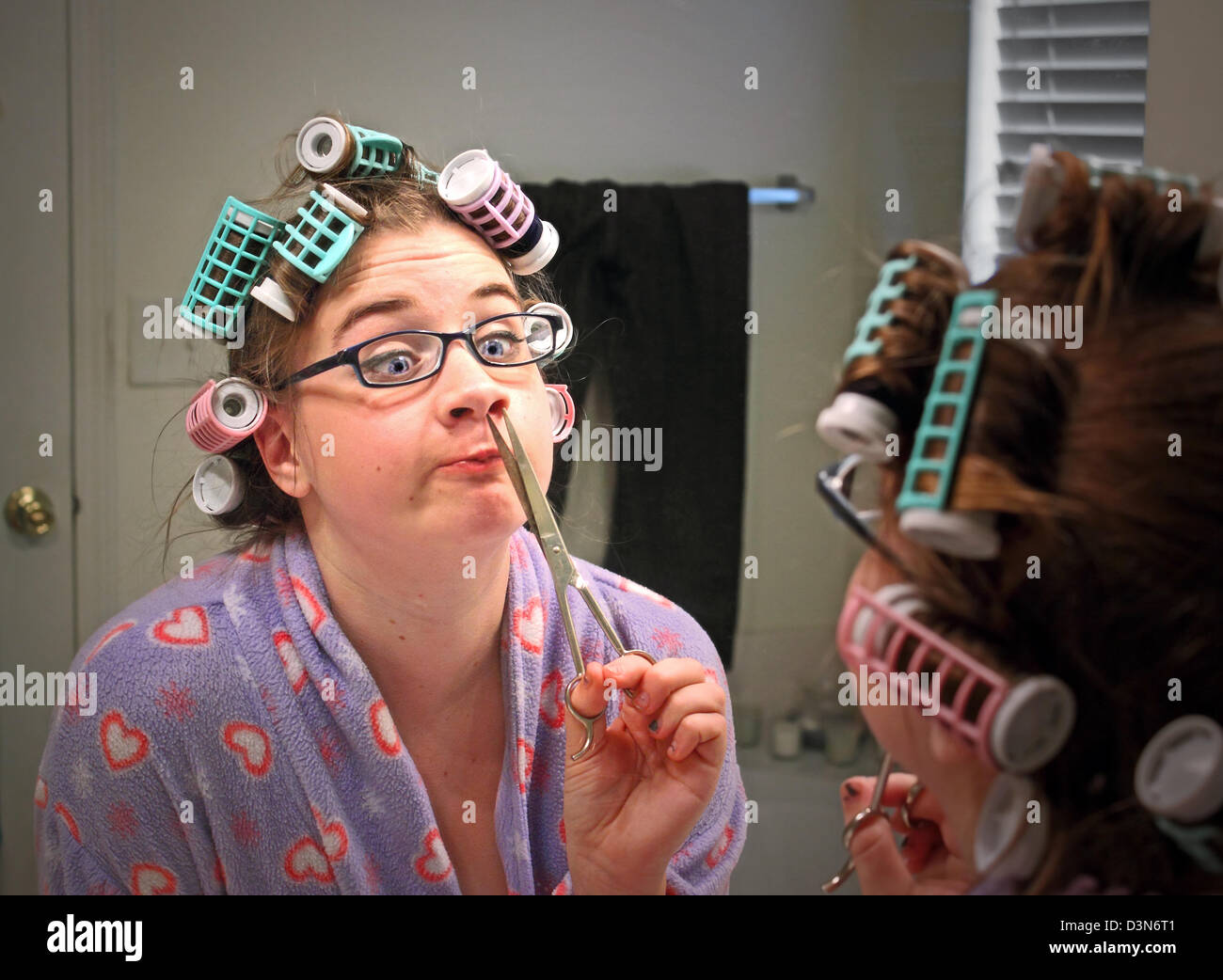 Una mujer joven con rulos y gafas hace una cara divertida al recortar su nariz pelos Foto de stock