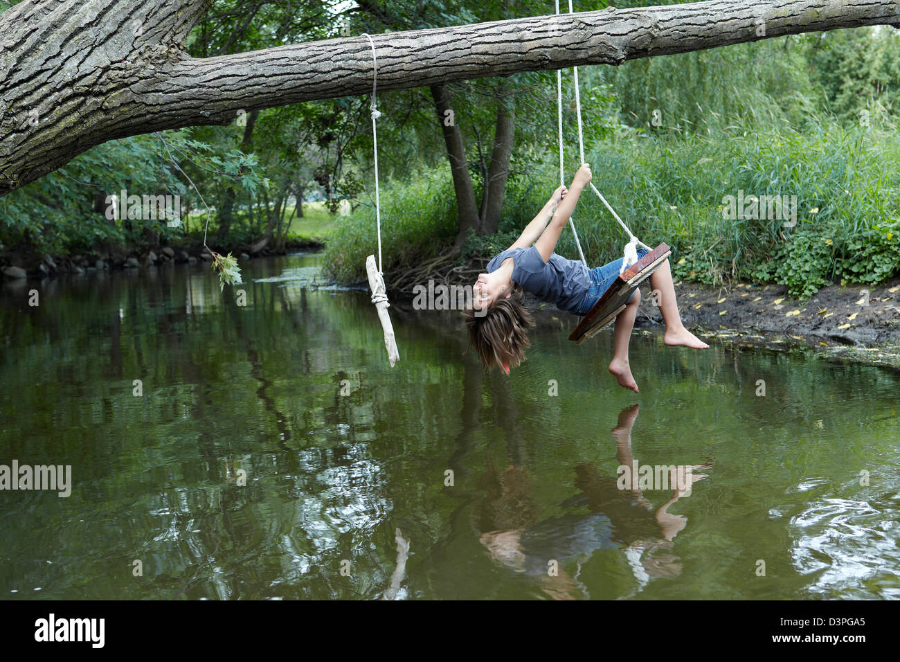 Niña de 9 años oscilando encima creek Foto de stock