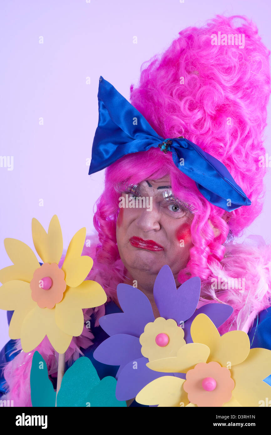 Expresión mueca de la pantomima dame en plástico jardín de flores o bouquet ricamente vestida en gran peluca rosa con lazo de seda azul Foto de stock