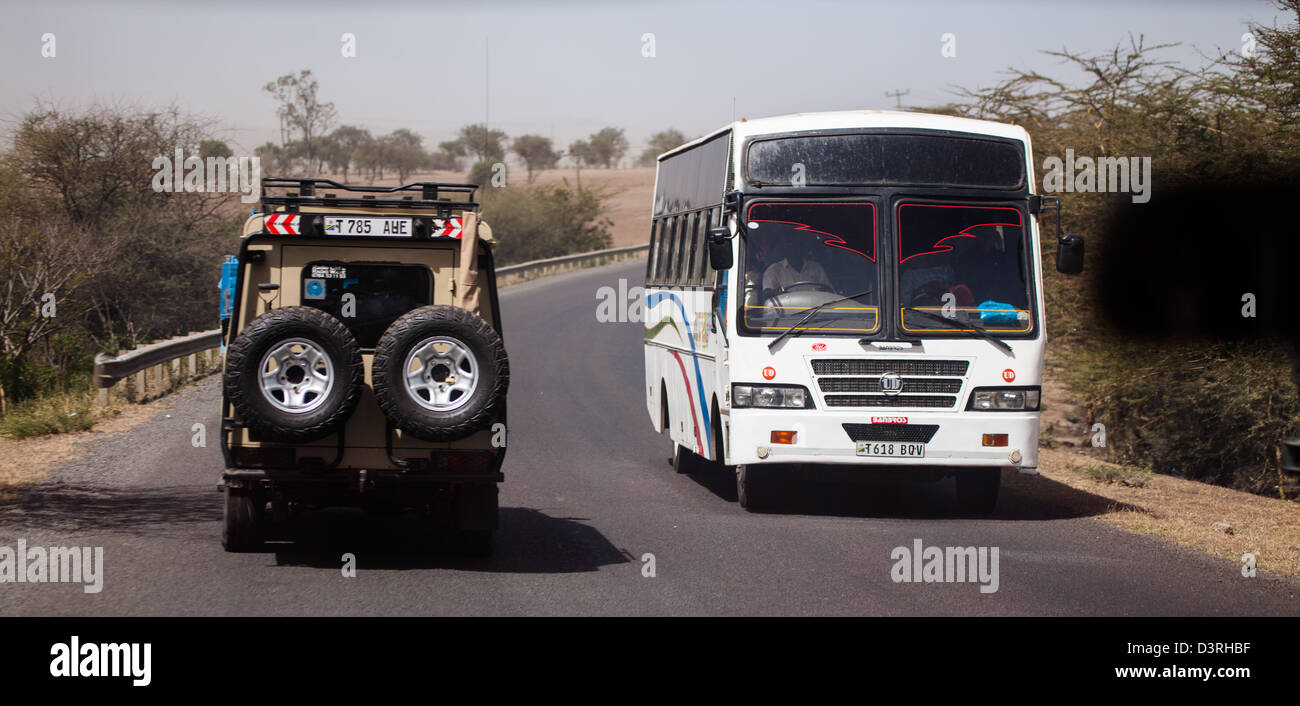 Un safari en jeep y un autobús lleno de lugareños pasan sobre la carretera fuera de Arusha, Tanzania. Foto de stock
