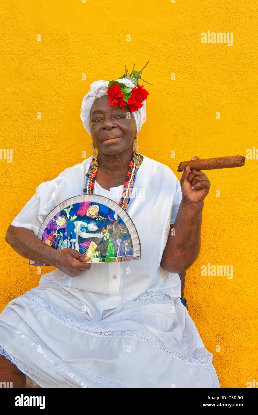 La mujer cubana de ascendencia africana vistiendo la Santería tradicional vestido blanco plantea en La Habana Vieja con cigarro y ventilador en mano La Habana Cuba Foto de stock