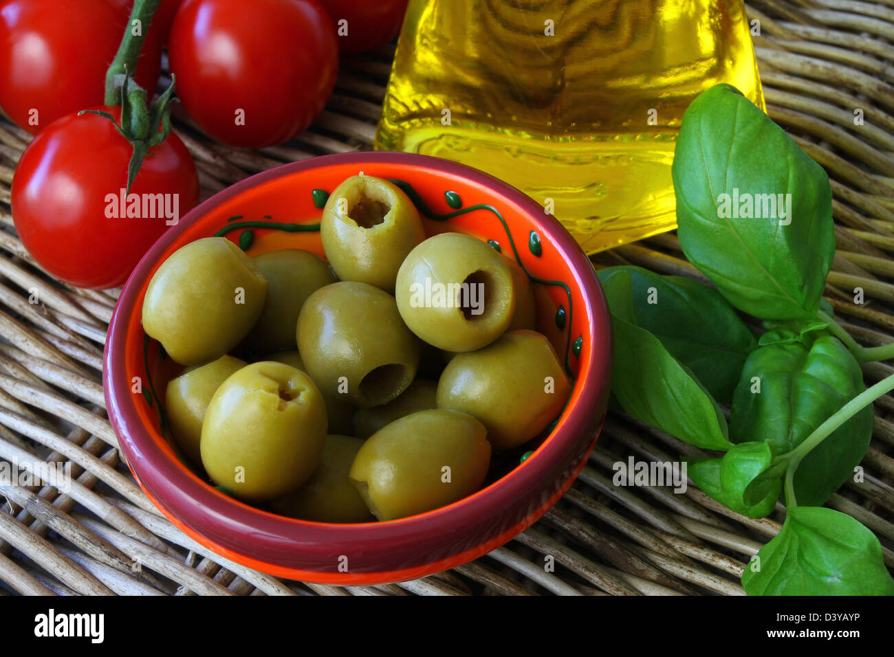 Aceitunas verdes, aceite de oliva, tomates cherry y hojas de albahaca fresca Foto de stock