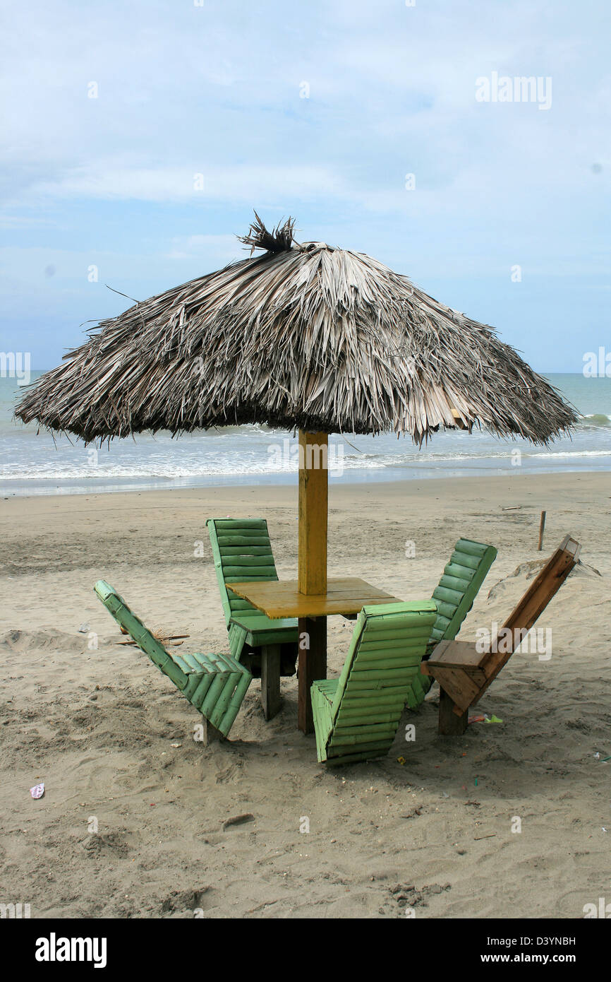 Una mesa y sillas de madera bajo una sombrilla de paja en una playa en la costa del Océano Pacífico en Tonsupa, Ecuador Fotografía de stock -