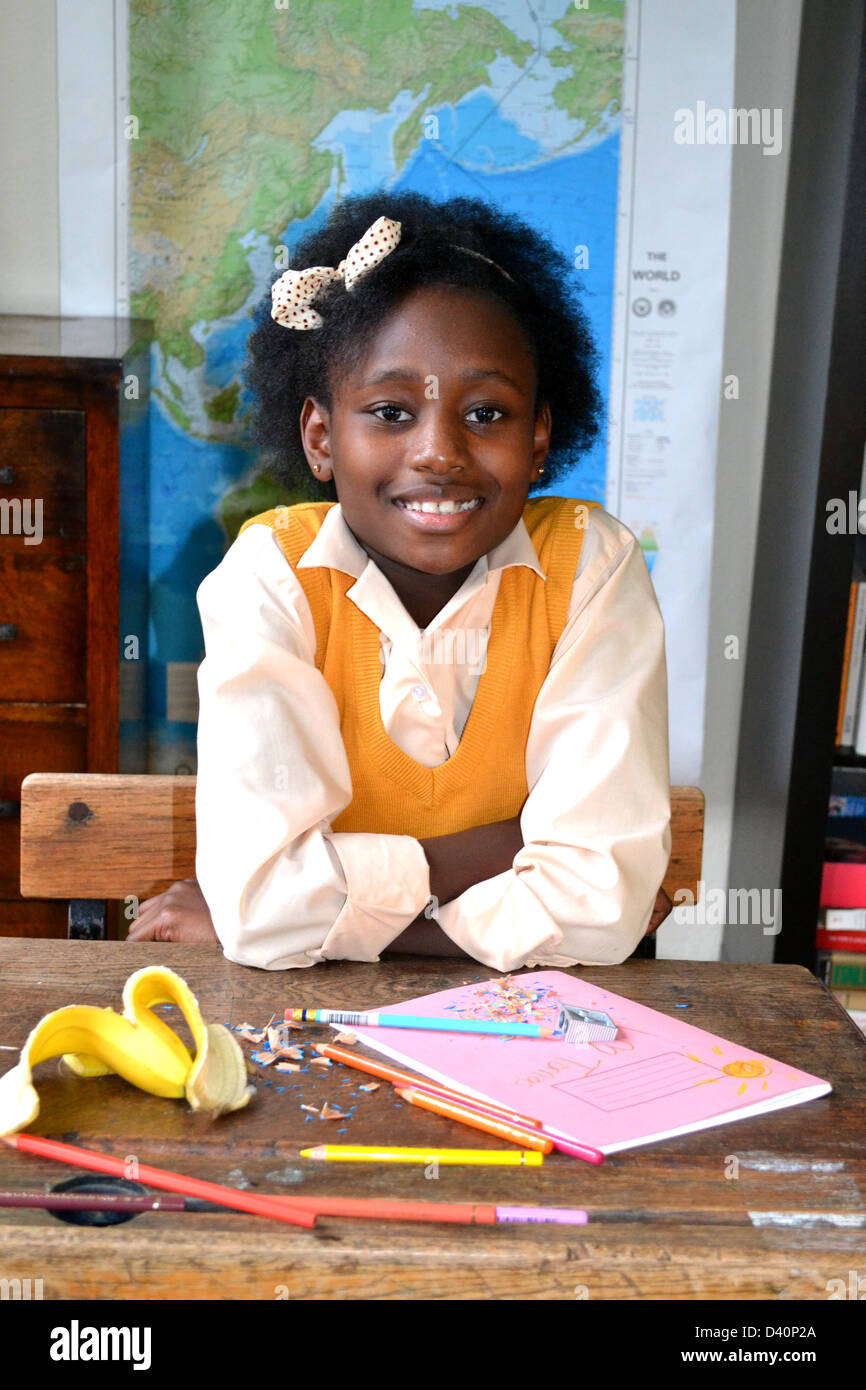 Dulce niña sonriente sentado en un escritorio desordenado en un aula. Foto de stock