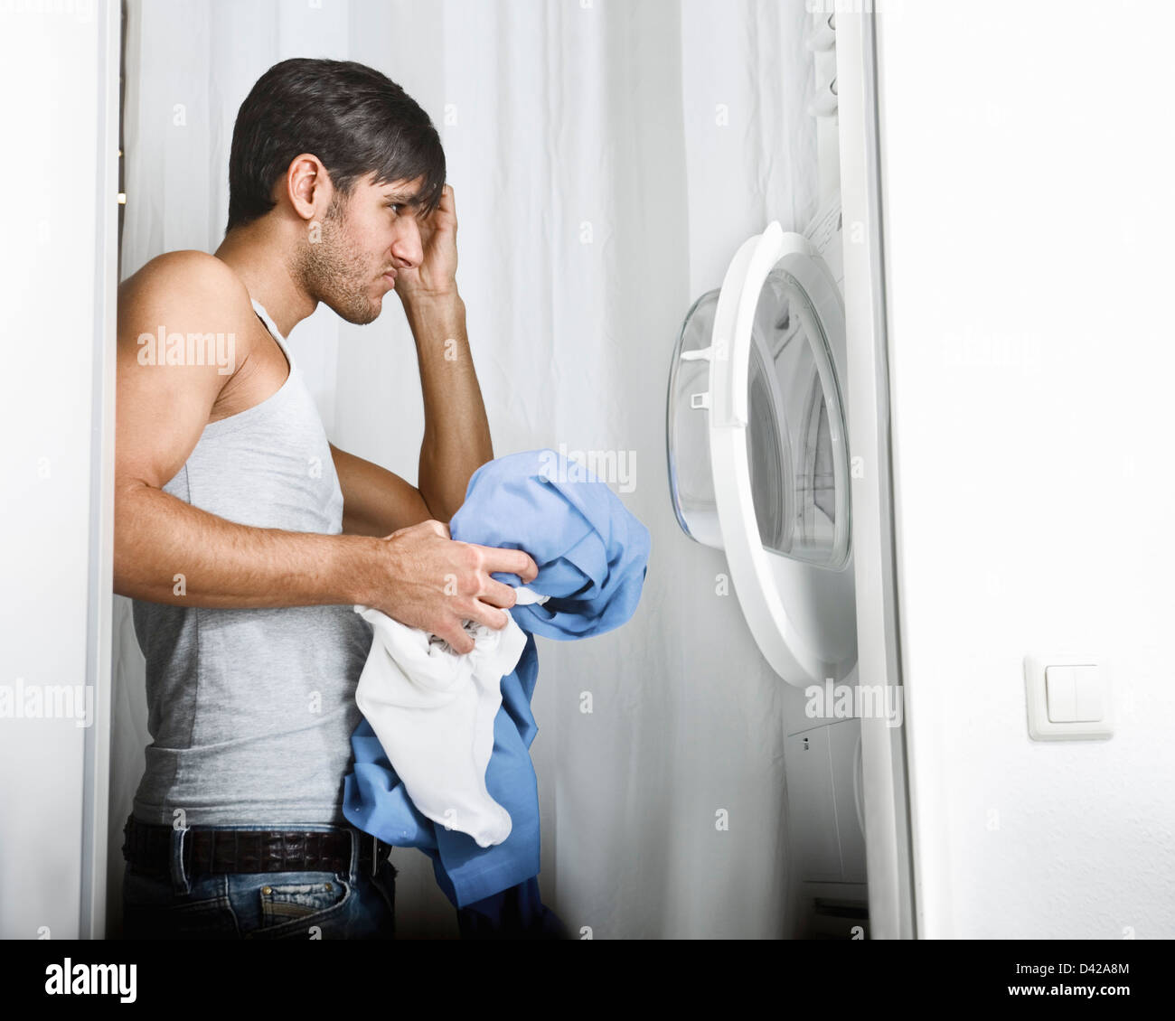Hombre teniendo problemas en el funcionamiento de la lavadora en la lavandería del día Foto de stock