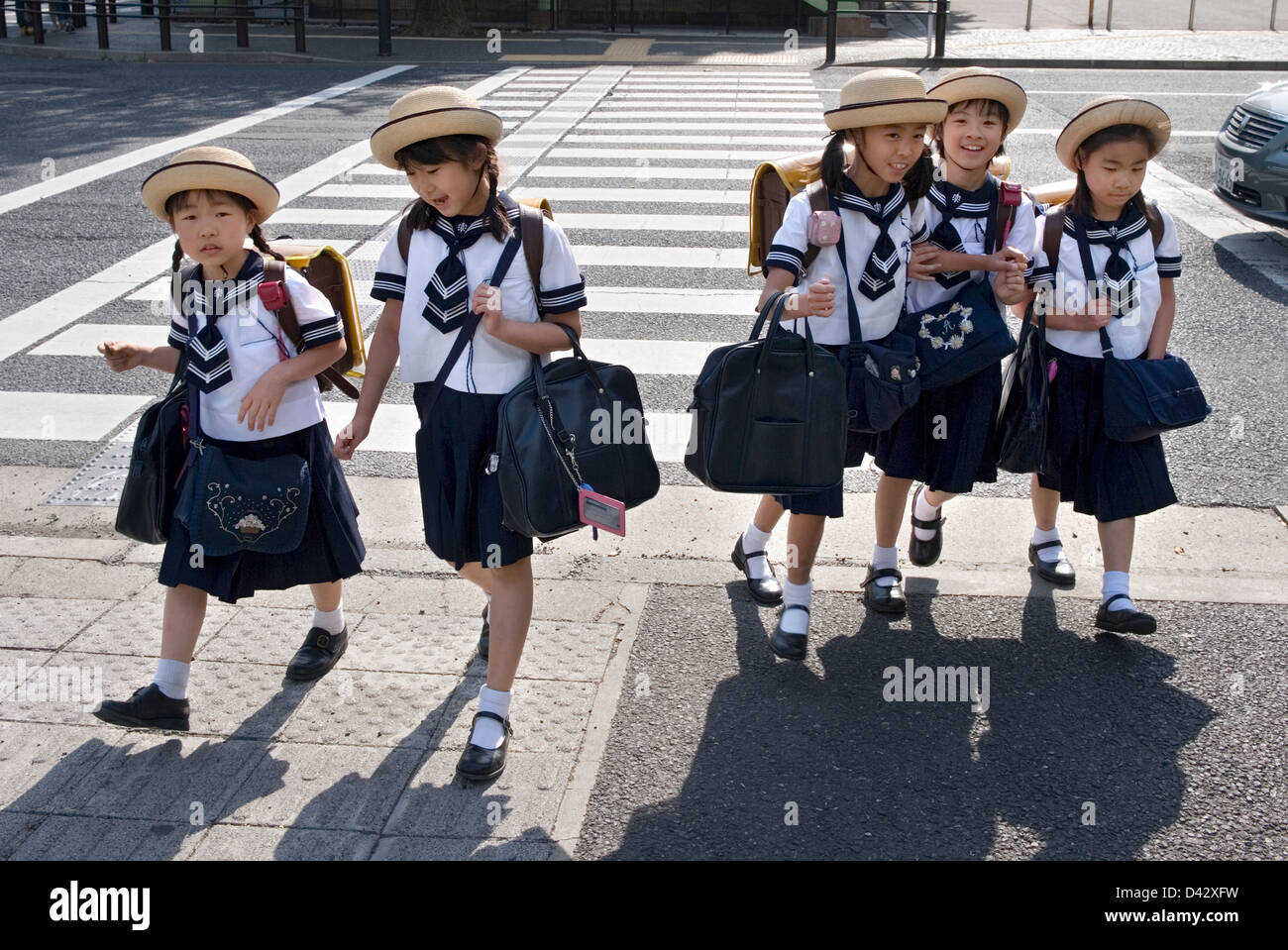 Cinco niñas de escuela primaria en sailor uniformes y sombreros lindo cruzar la calle en su camino a casa desde la escuela en Tokio. Foto de stock