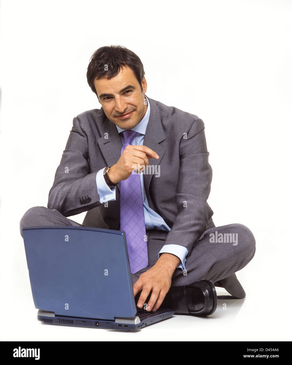 Stdio retrato de hombre de negocios palo atar el collar blanco traje de dos piezas y sentados en el suelo con su ordenador portátil sonriendo Foto de stock