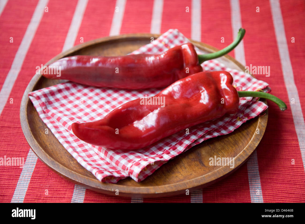 Dos italianos Romano señaló pimientos uno al lado del otro en una placa de madera con una casilla roja serviette y mantel de rayas. Foto de stock